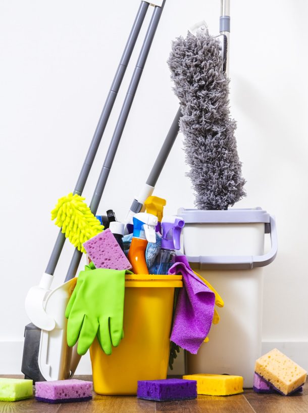 Cleaning products, household chemicals bottles and sprays, rags, sponges in orange bucket for washing the floor, brushes, broom for wiping and dusting